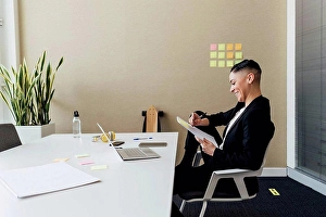 Business Women Prints: Smiling businesswoman writing on paper while sitting at desk in office