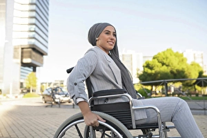 Disability Prints: Smiling disabled woman sitting on wheelchair at footpath