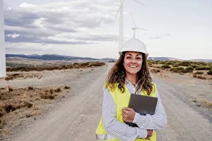 Competence Prints: Smiling engineer wearing hardhat holding laptop at wind farm
