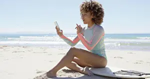 Browsing Prints: Smiling female on beach using smartphone Smiling female sitting on surfboard on beach using smartphone on sea