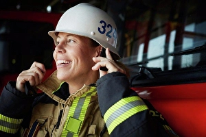 Business And Occupation Prints: Smiling female firefighter wearing helmet at fire station