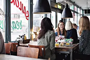 Occasion Prints: Smiling female friends enjoying while sitting at dining table for brunch in restaurant