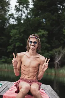 Kindness Prints: Smiling fit queer young man sitting by lake at festival in Poland
