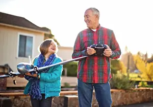 Conversation Prints: Smiling girl and her grandfather having fun playing with a toy airplane together in the back yard