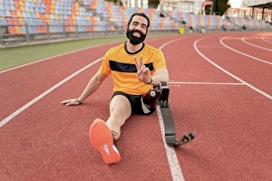 Handicapped Prints: Smiling man with prosthetic leg sitting on running track showing peace sign