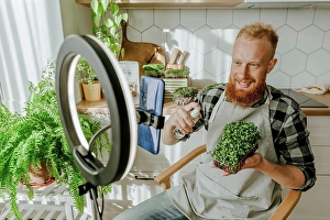 Using Phone Prints: Smiling man spraying water on microgreens sitting in front of smart phone