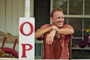 50 To 55 Years Prints: Smiling mature store owner relaxes on the veranda of his antiques shop