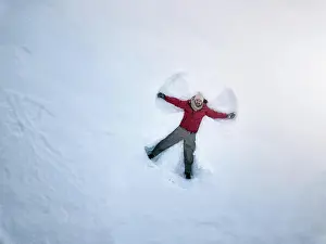 Frosty Prints: From above smiling middle-aged male in outwear lying on white snow and making snow angel silhouette