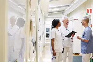 Doctors Prints: Smiling multi-ethnic doctors discussing while standing in hospital corridor