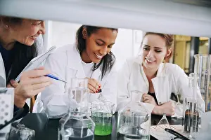Instruction Prints: Smiling multi-ethnic university students with mature teacher mixing solution in laboratory