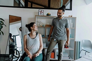 Handicapped Prints: Smiling physiotherapist with female patient sitting on wheelchair in medical practice