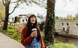 35 To 40 Years Prints: Smiling woman holding coffee cup and listening to music through wireless headphones