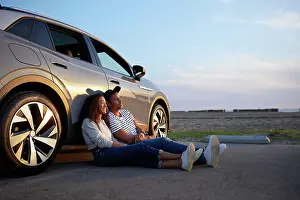 Sustainable Energy Prints: Smiling woman sitting with boyfriend against car during sunset