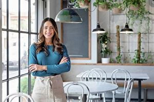 Head On Prints: Smiling woman standing with arms crossed in cafe