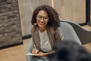 Notes Prints: Smiling woman writing something down while sitting with colleague in modern office