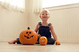 3 4 Years Prints: Smiling, young boy sits a floor behind a big Jack O'Lantern