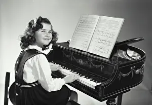 Grand Prints: Smiling young brunette caucasian girl wearing dress sitting at petite grand piano with sheet music with head turned to
