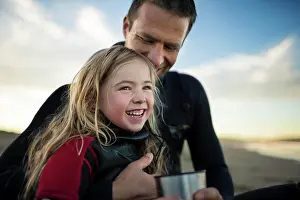 30 To 35 Years Prints: Smiling young girl and her father share a hot drink as they relax on the beach after a long day
