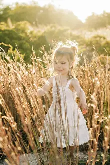 1 2 Years Old Prints: Smiling young girl in a white dress walking through tall grass