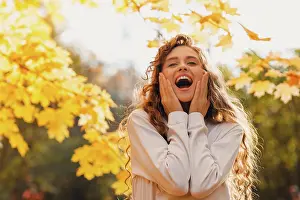 Draussen Prints: Smiling young woman enjoy the autumn weather in the parkland with the yellow leaves at branches