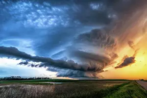 Dangerous Prints: Spinning mesocyclone tornado warned storm over rural gravel road and field at sunset in Saskatechewan Canada