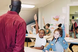 Communications Prints: Students raising hand while looking at teacher in classroom at school