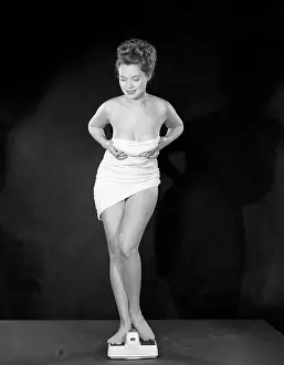 One Young Woman Only Prints: Studio portrait of naked young woman holding towel on scales