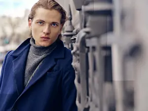 Thoughtful Prints: stylish young male with trendy hairstyle dressed in elegant coat standing against gray stone wall in city