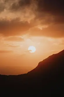 Dramatic Sky Prints: Sunset in orange sky above silhouetted cliff and sea, Klakkur, Klaksvik, Faroe Islands