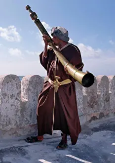 Muslim Prints: A Swahili man in traditional attire blows the Siwa on the battlements of the Lamu Museum