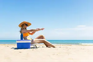 Bikini Prints: a tanned girl in a swimsuit, hat and glasses sits on a sun lounger smears sunscreen on her hands
