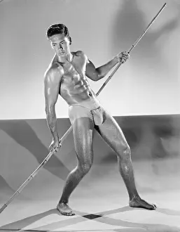 Bodybuilder Prints: Tanned Muscular Bodybuilder Poses with Staff c.1953