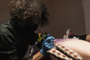 Anonymous Prints: Tattooist working with client in salon