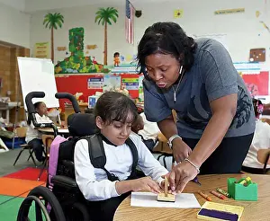 Students Prints: A teacher helps a girl in a wheelchair in a classroom at Oakman Elementary school; teachers