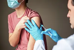 Physician Prints: Teen boy wearing mask getting vaccinated by doctor holding a needle