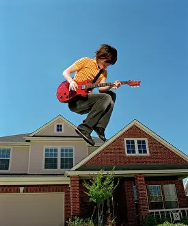 Hobbies Prints: Teenage boy with guitar jumping in front of home, striking a pose mid air