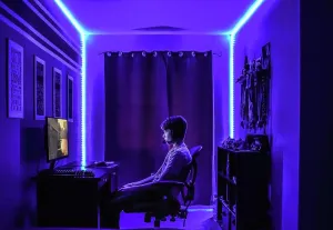 Video Prints: Teenage boy playing video game at desk in room with neon LED lighting