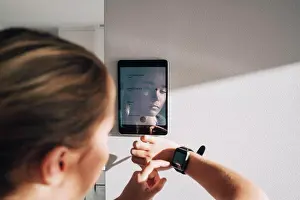 Adjusting Prints: Teenage girl adjusting smart watch with digital tablet mounted on white wall at home