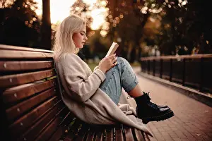 Sweater Prints: Teenage girl reading book sitting on bench in park during autumn