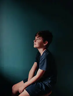 Thoughtful Prints: Thoughtful young boy sitting on a stool against a dark blue wall