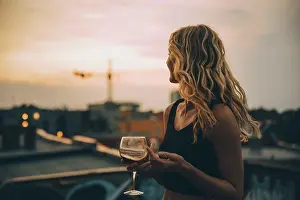 Frgbild Prints: Thoughtful young woman having wine while looking away on terrace during rooftop party at sunset