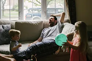 Small Group Prints: A tired father lies on the couch while his children play around him