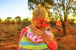 Hair Bun Prints: Tourist woman holding and kissing kangaroo joey at sunset light in Australian Outback