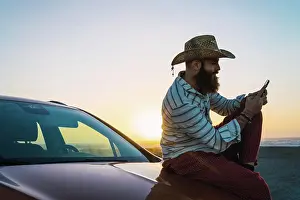 Pensive Prints: Traveler sitting on car browsing smartphone