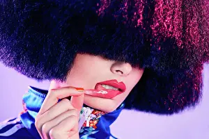Individuality Prints: Trendy female in lavish wig removing glossy sticker from lip under magenta light against violet background