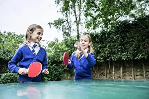 Twin girls in school uniform playing table tennis outside