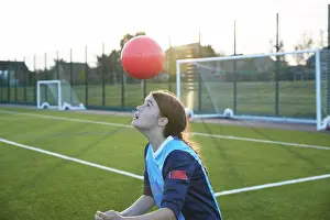 Outdoor Pursuit Prints: UK, Female soccer player bouncing ball in field at sunset