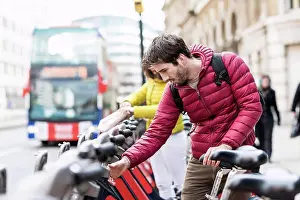 Bicycle Prints: UK, London, young man renting bicycle from bike share stand in city