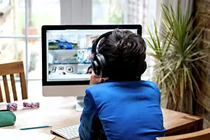 Desk Prints: UK, Rear view of boy with headphones sitting in front of computer