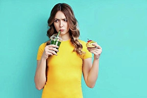 Expressions Prints: Unhappy woman on dieting drinking detox juice holding cake in hand choosing healthy food